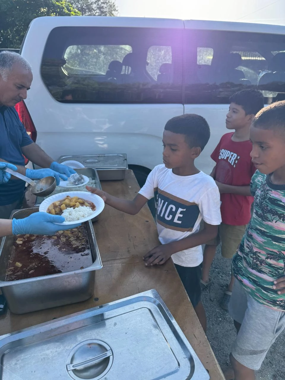 A volunteer in blue gloves hands a plate of rice and stew to a young boy